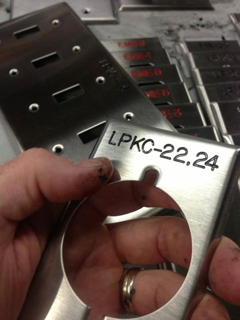 Hand holding engraved stainless device plate labeled LPKC-22.24